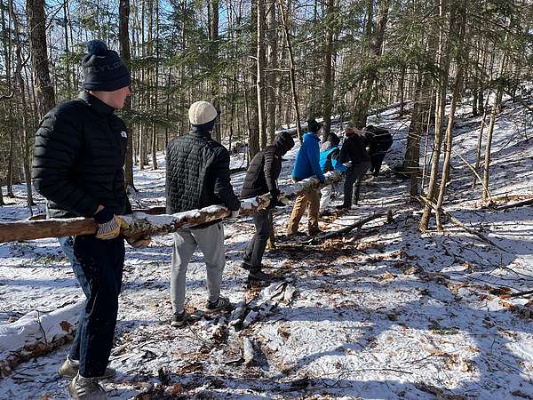 A group of students work together to carry a down tree away from the trail corridor.